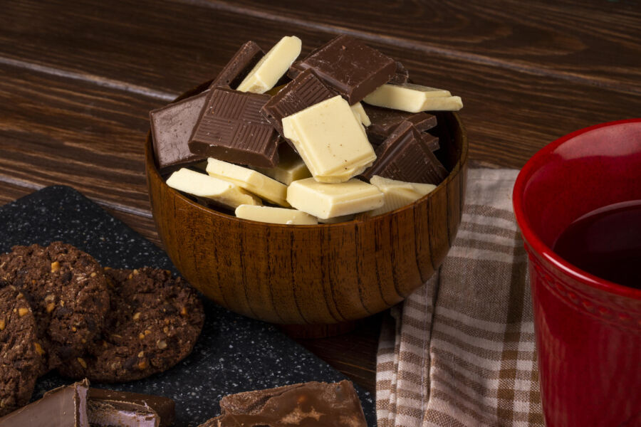 Imagem vista-lateral-de-uma-caneca-com-biscoitos-de-aveia-cha-e-pedacos-de-chocolate-escuros-e-brancos-em-uma-tigela-de-madeira-no-fundo-rustico